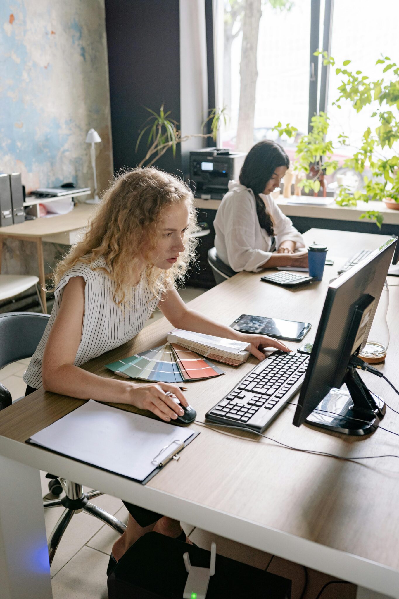 Two women focused on work at a desk, showcasing a vibrant and collaborative office environment.